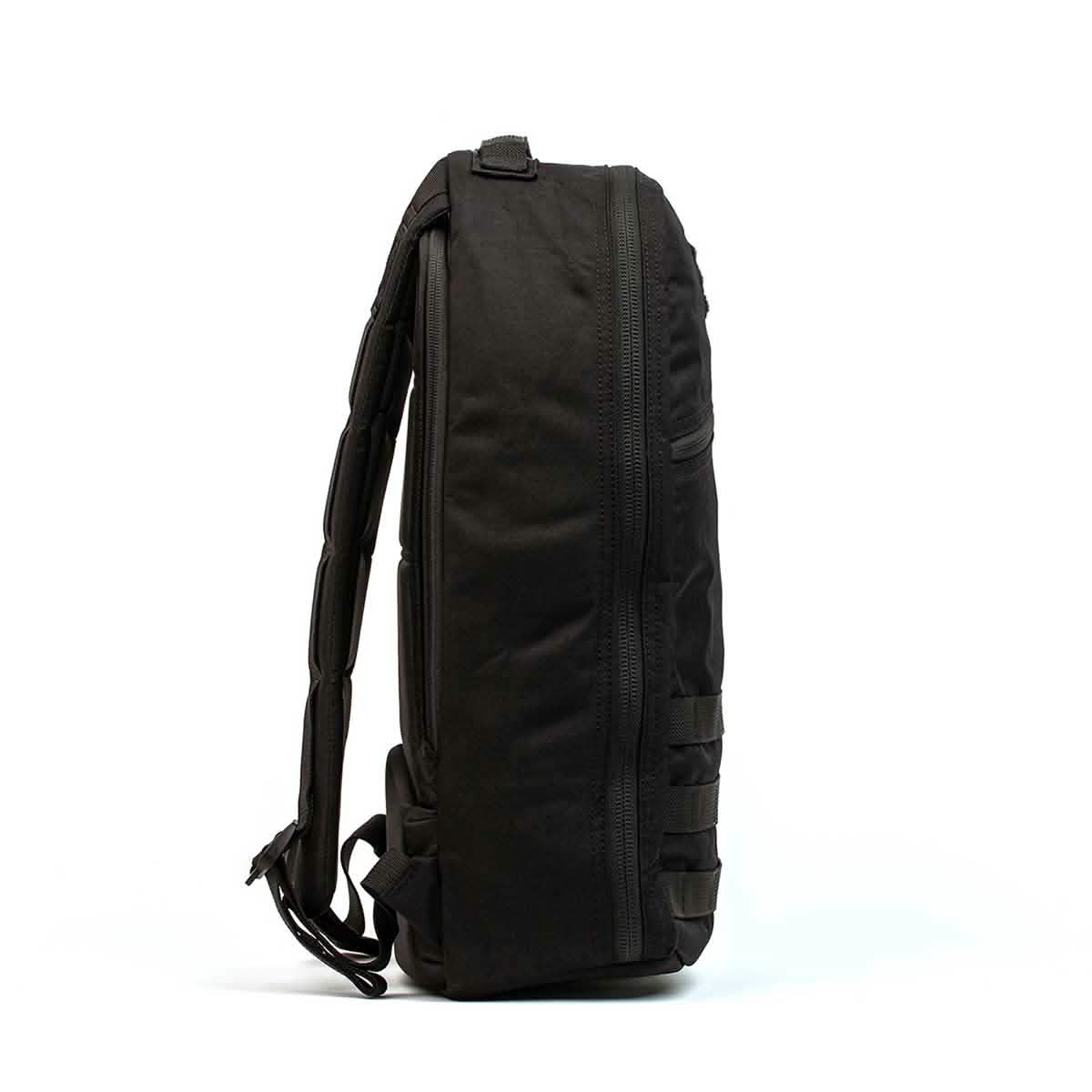 Side view of the GORUCK Bullet Ruck Laptop - 16L backpack in black, showcasing several horizontal straps and a zipper extending down its length. It is designed for functional carrying and storage, featuring a laptop compartment, padded back, lumbar support, and adjustable shoulder straps.