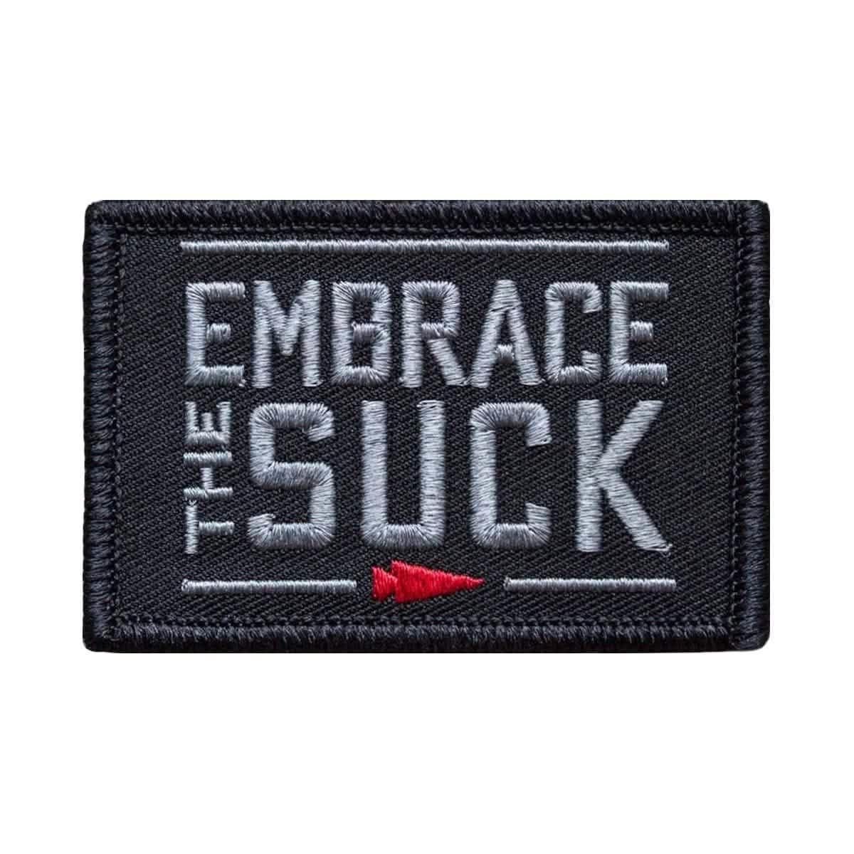 Black embroidered patch with white text 'Embrace The Suck' and a small red arrow emblem