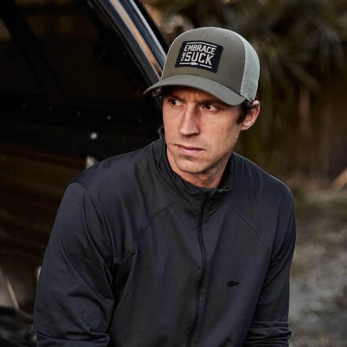 Man wearing GORUCK Embrace the Suck hat and black jacket outdoors