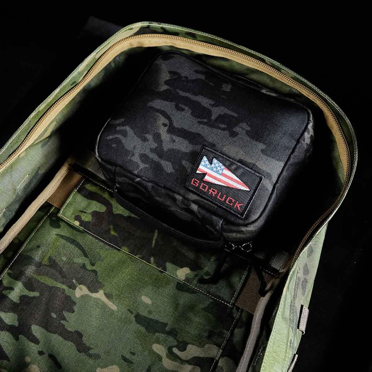 Black GORUCK pouch with American flag patch inside green camouflage rucksack open against black background
