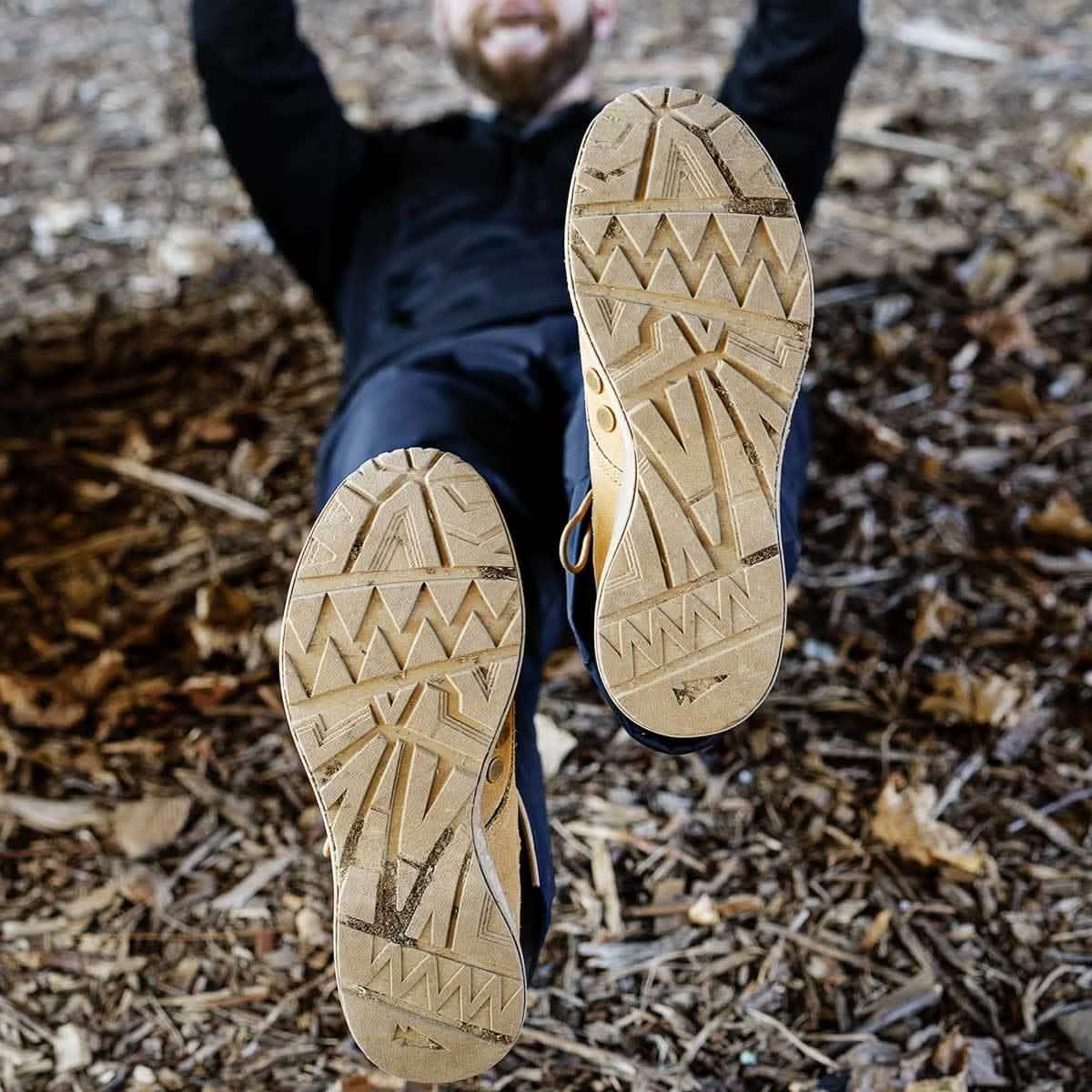 Close-up of tan suede GORUCK MACV1 boot soles with rugged tread pattern against wood chip ground