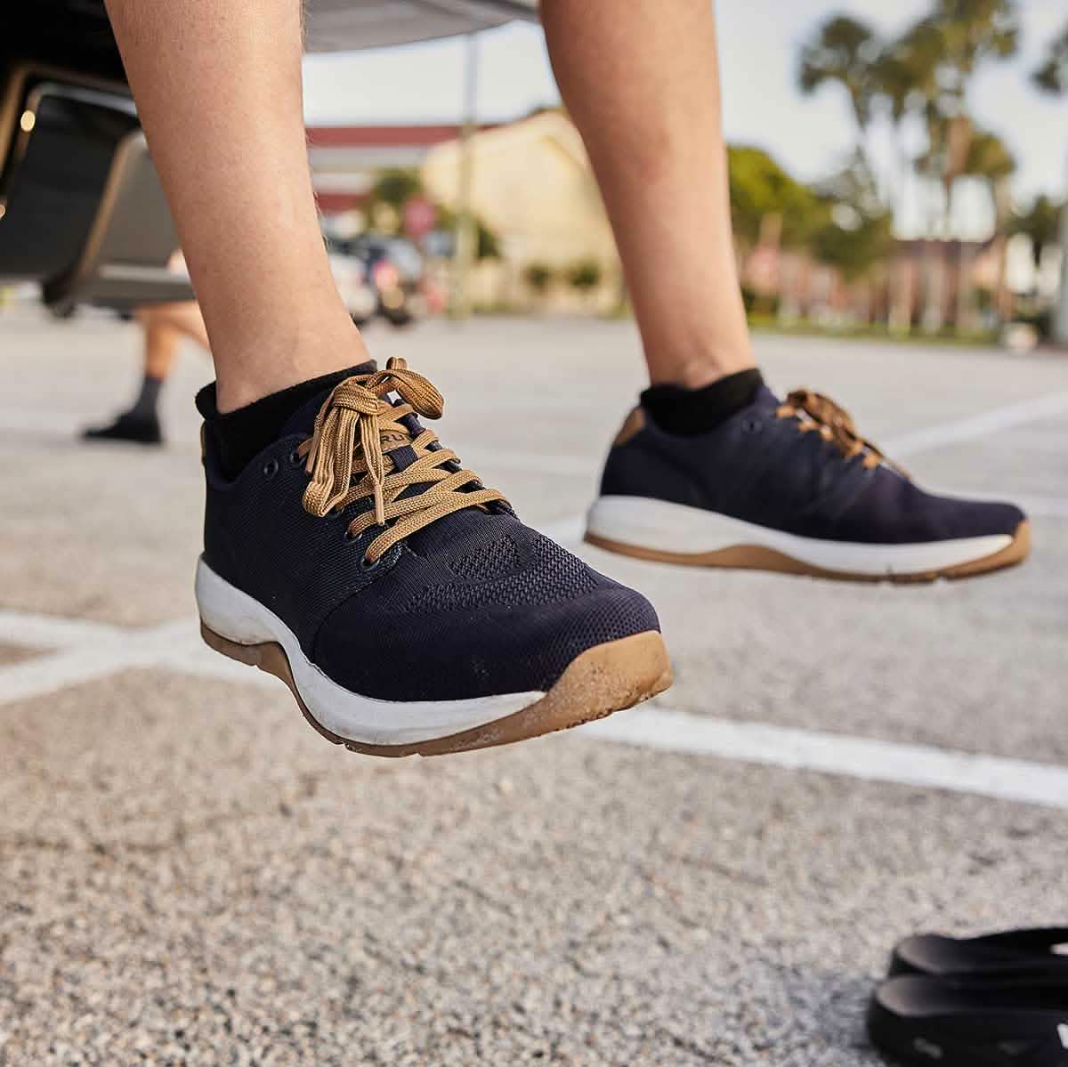 Close-up of a person wearing Ballistic Trainers in Navy + White + Coyote, stepping onto parking lot pavement to highlight the shoes’ stability support.