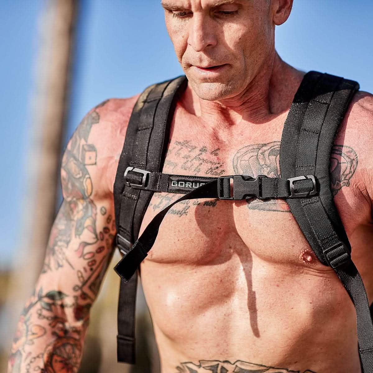 Close-up of muscular man wearing GORUCK black sternum strap with tattoos in outdoor rucking gear