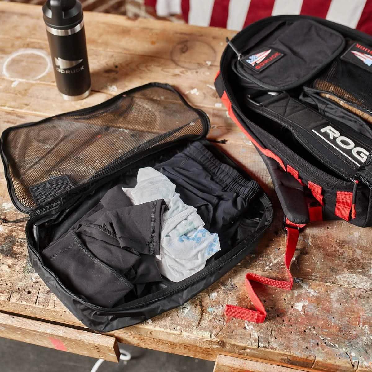 GORUCK 10L packing cube open with folded clothes beside rucksack and water bottle on wood table