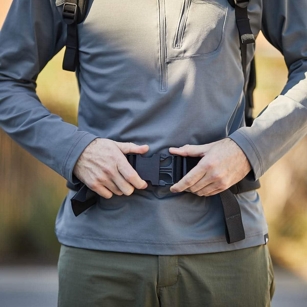 Close-up of person fastening padded hip belt buckle on black backpack straps, outdoors in daylight