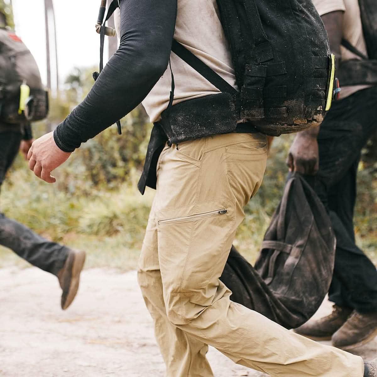 Close-up of a person wearing a padded hip belt with a black backpack and beige tactical pants during an outdoor rucking event