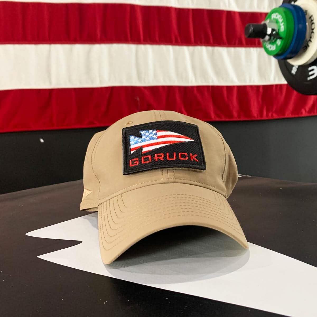 Coyote tan GORUCK performance tactical hat with American flag patch on black table in front of American flag backdrop