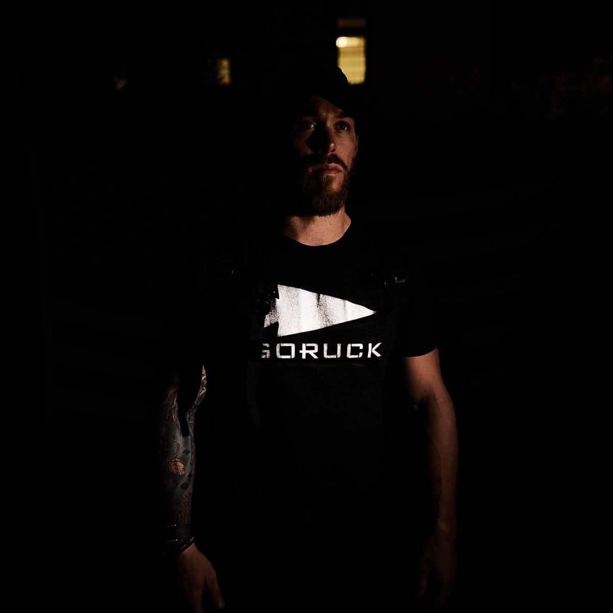Man wearing black GORUCK reflective tee in low light, showing rucking gear logo.