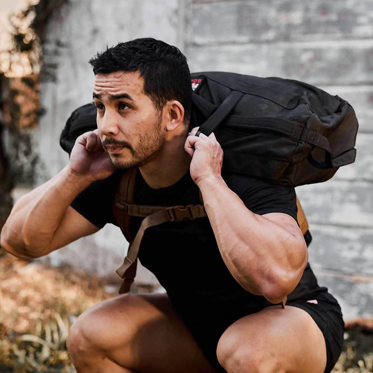 Athlete performing squat outdoors carrying heavy black GORUCK sandbag on shoulders