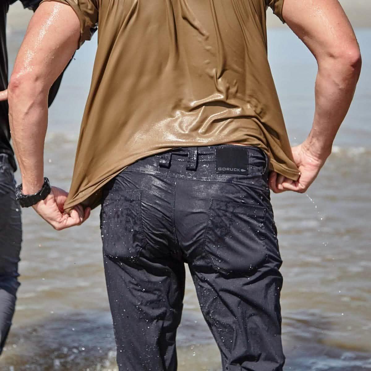 Person wearing wet GORUCK black simple pants and a brown shirt near water, showcasing durable rucking gear