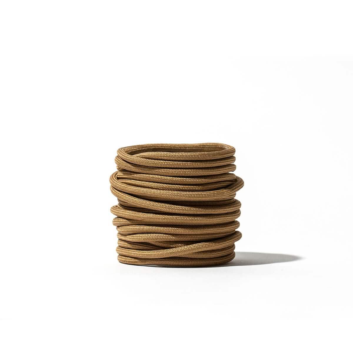 A stack of neatly coiled GORUCK Speed Laces, featuring a 3mm thickness in brown, set against a white background with their shadow visible on the surface.