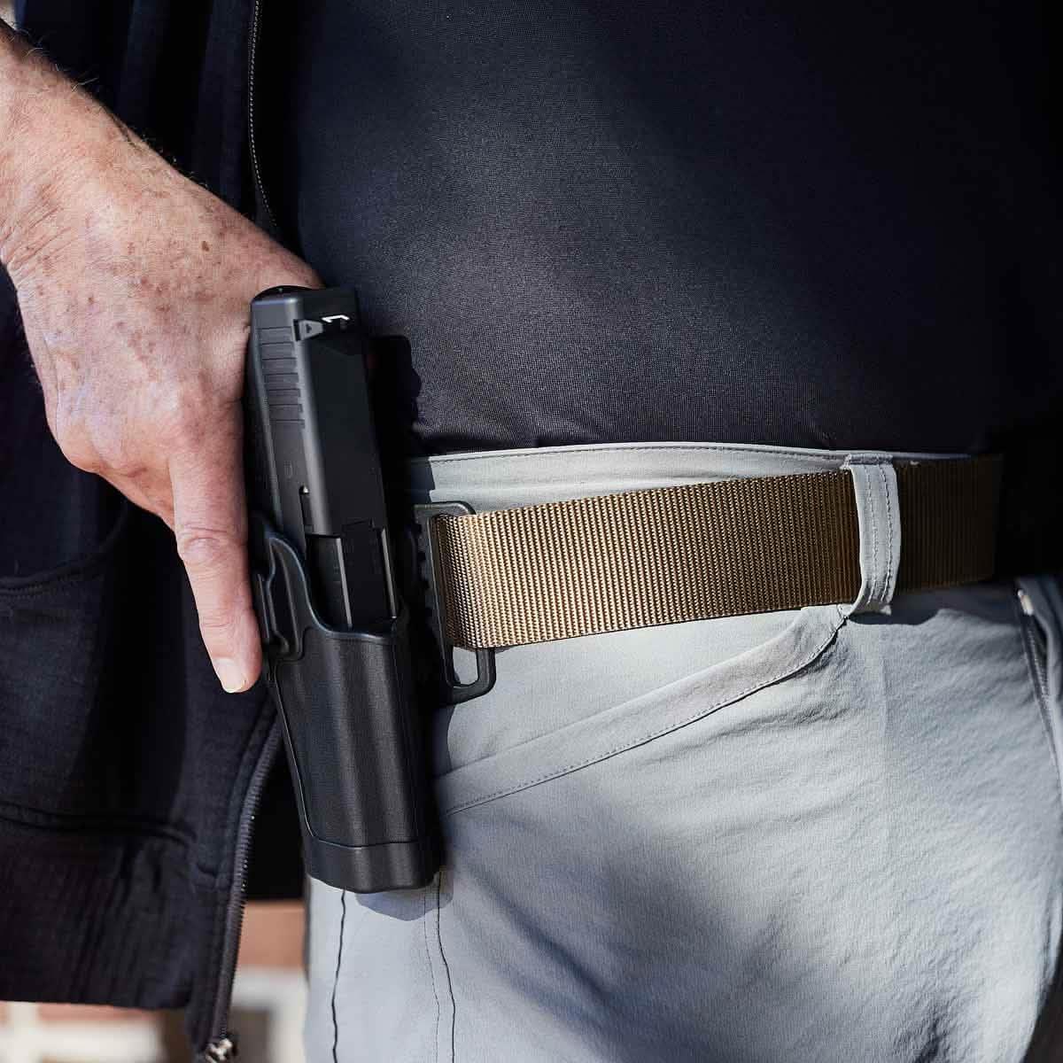Person wearing tactical coyote belt with pistol holstered on hip, showcasing durable rucking gear