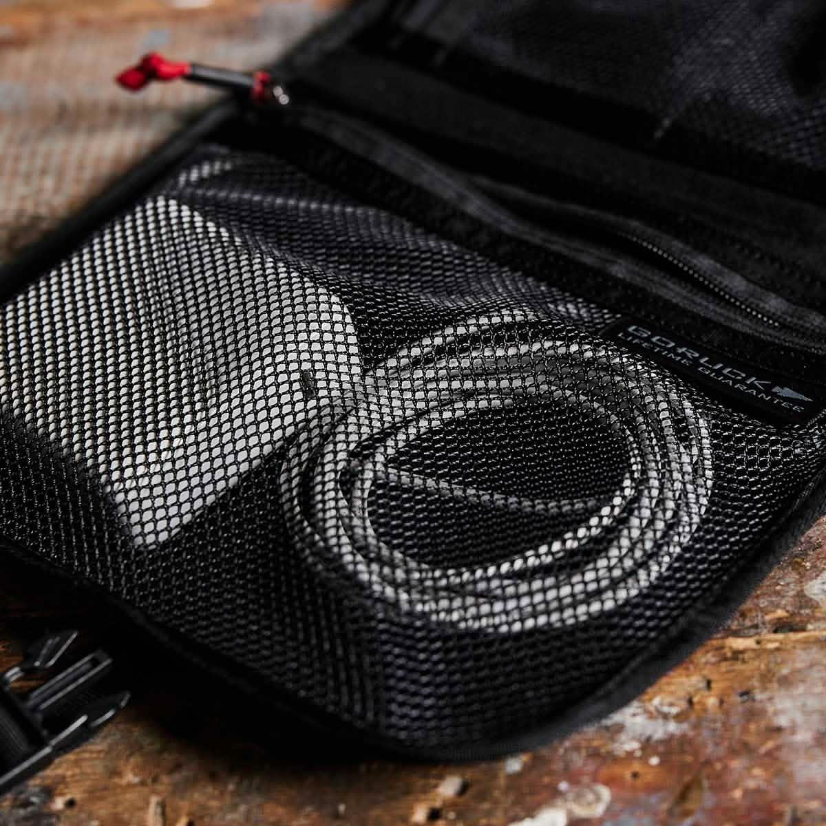 GORUCK black mesh pocket organizer holding white charger and coiled cable on rustic surface