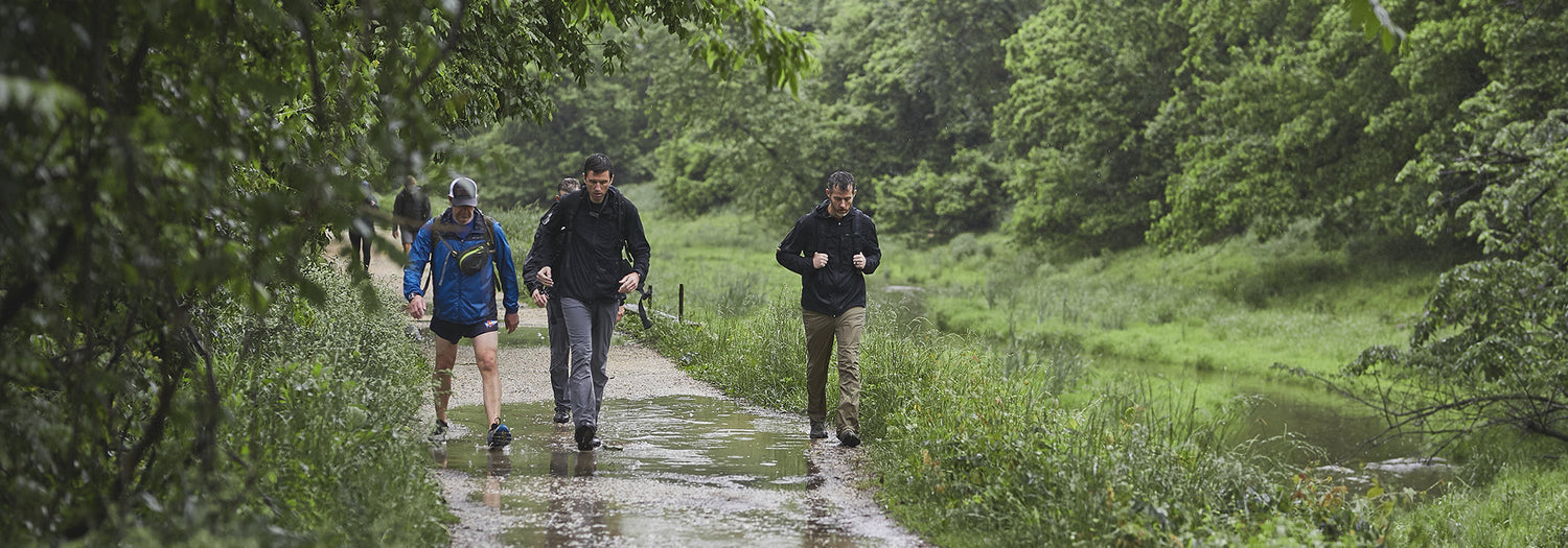 GORUCK rucking gear in action as people hike a wet forest trail, rugged outdoor fitness