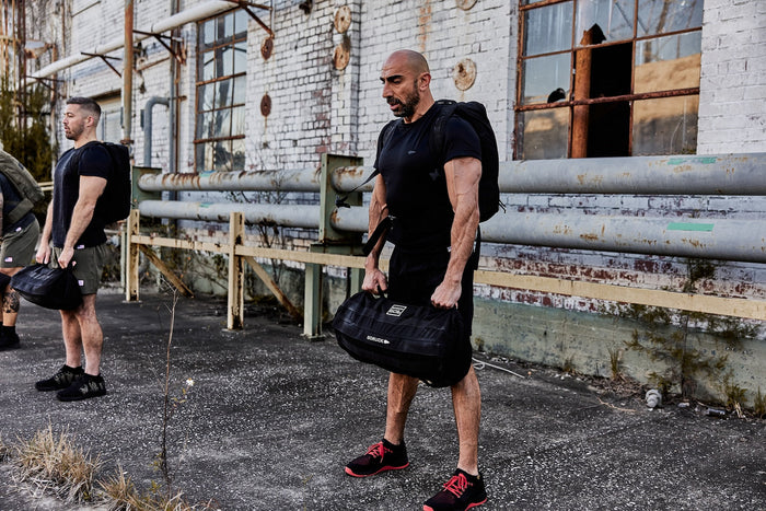 Men training outdoors with GORUCK rucksacks and sandbags by an industrial building