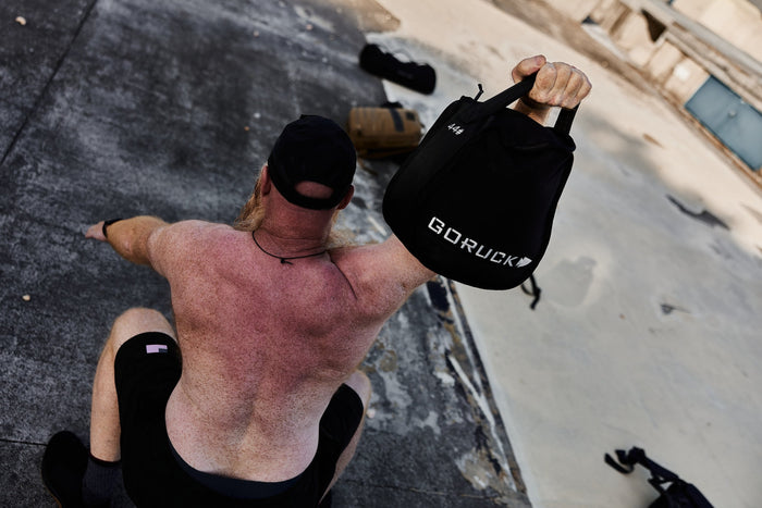 Man performing outdoor workout holding GORUCK sandbag, showcasing rucking fitness gear