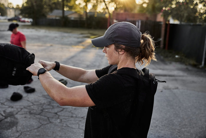 Woman training outdoors with GORUCK ruck gear and sandbag at sunset