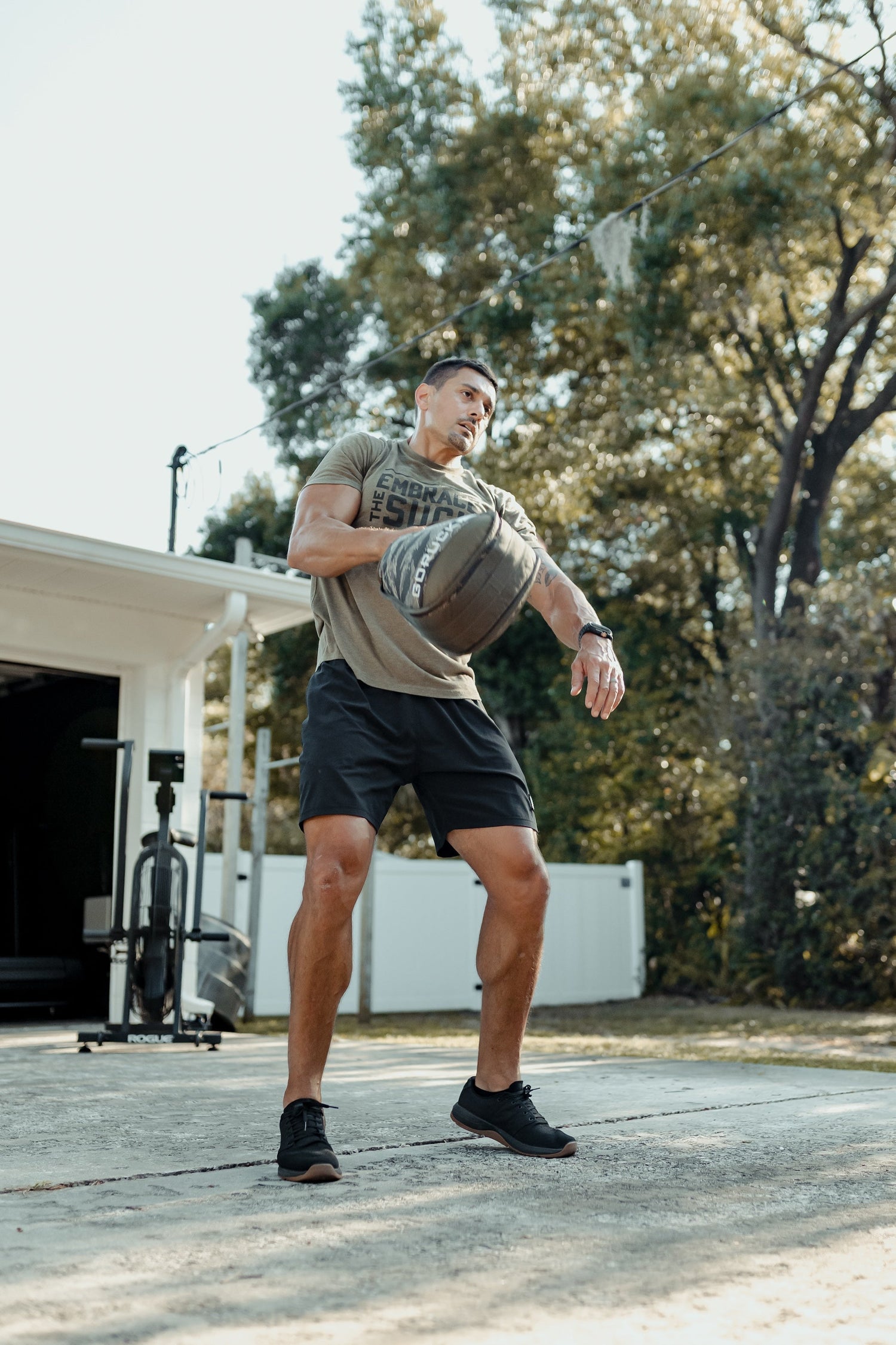 Man training outdoors with GORUCK sandbag, wearing athletic gear and GORUCK t-shirt.