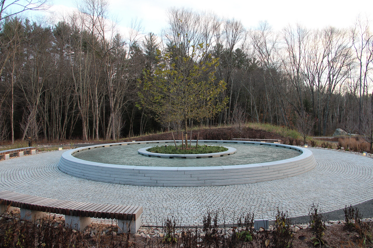 Sandy Hook Memorial with circular water feature and central tree surrounded by benches in autumn forest