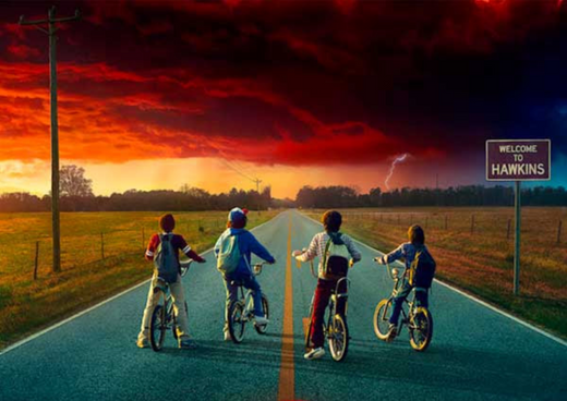 Four kids on bikes facing a stormy red sky on a rural road with a Welcome to Hawkins sign
