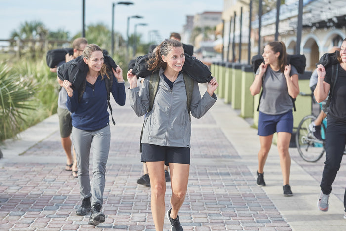 Group of people rucking with sandbags on a sunny boardwalk, wearing GORUCK gear