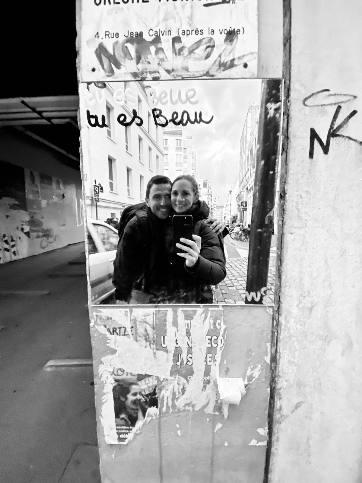 Black and white photo of a couple taking a mirror selfie on Rue Jean Calvin with graffiti on the mirror