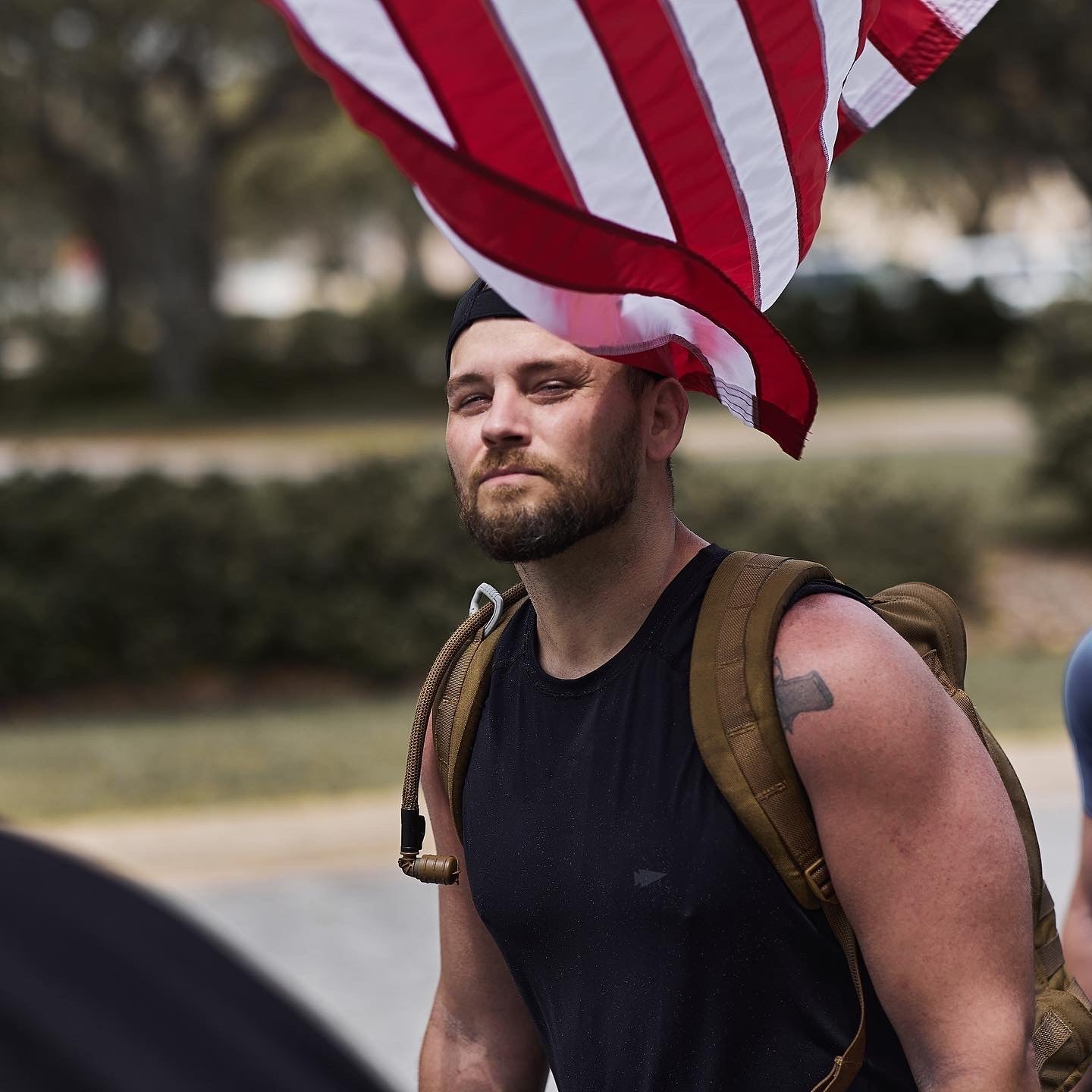 Man rucking outdoors with backpack and American flag, GORUCK event community fitness
