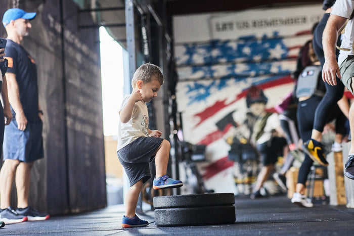 Child stepping on stacked weights in GORUCK gym with American flag wall mural