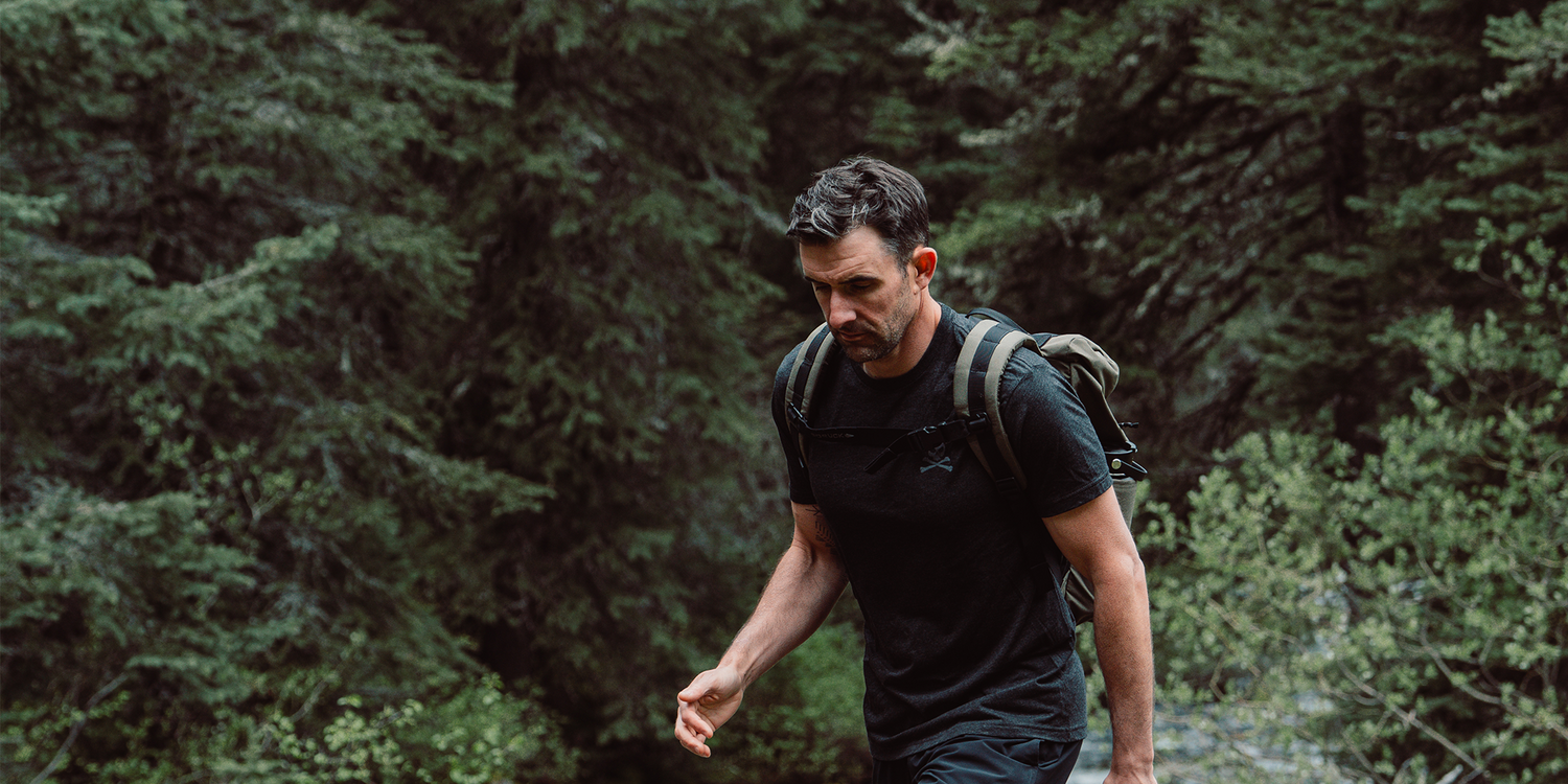 Man hiking in dense green forest wearing black t-shirt and backpack