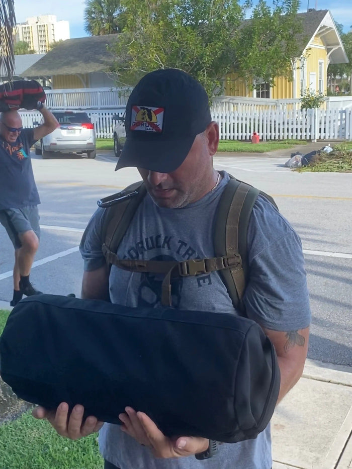 Man wearing GORUCK Tribe shirt and GORUCK Club hat carrying ruck sack outdoors