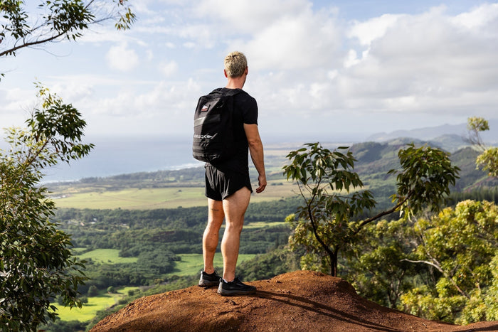 Man wearing GORUCK backpack overlooks scenic lush valley and ocean from a Hawaii trail