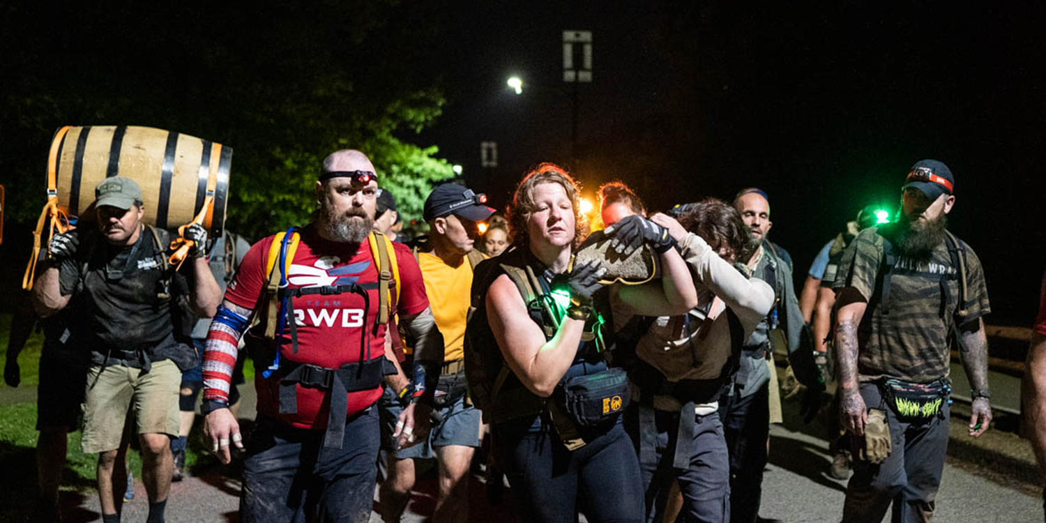 Group of people carrying a large barrel and walking at night wearing athletic gear and headlamps