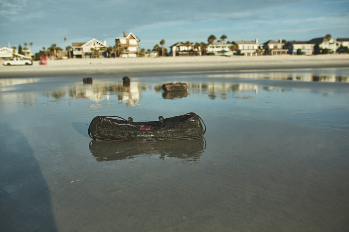 GORUCK sandbag on wet beach with coastal homes in background, rucking gear for outdoor training