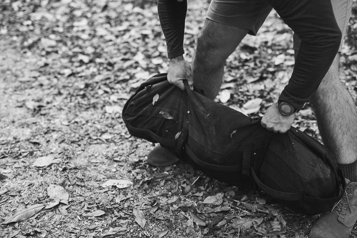 Person lifting GORUCK rucking sandbag outdoors on a leaf-covered trail