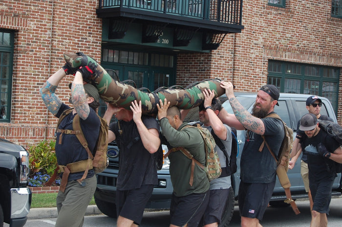 Group of men in tactical gear carrying a camouflage weighted training dummy during GORUCK event outdoors