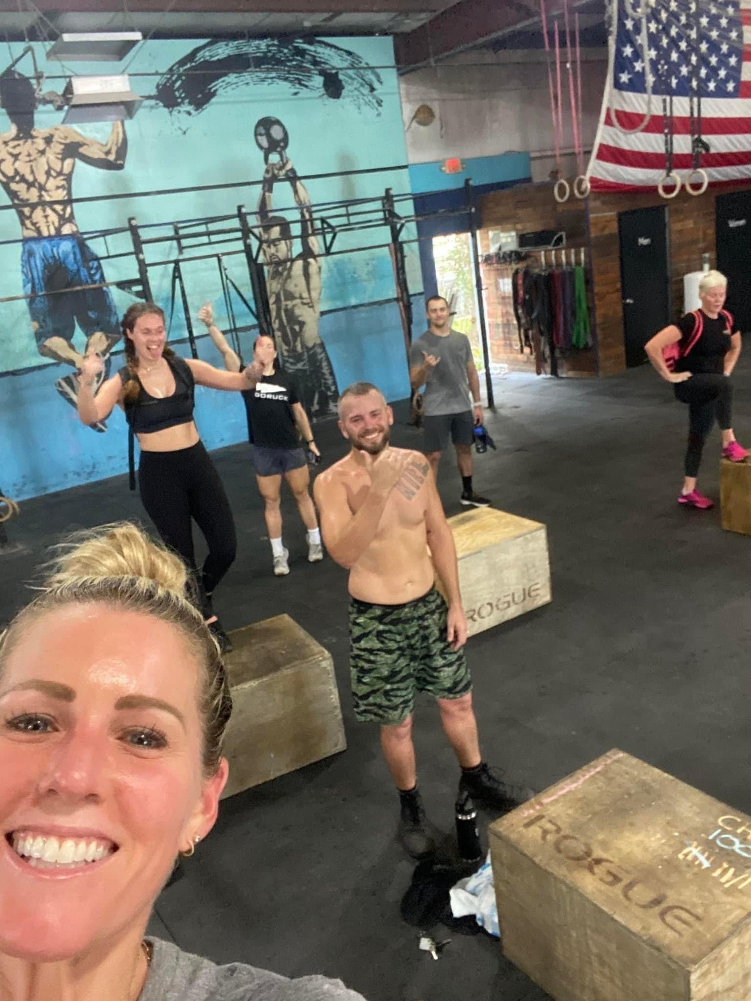 GORUCK rucking group in a gym with box jumps, American flag, and fitness mural background