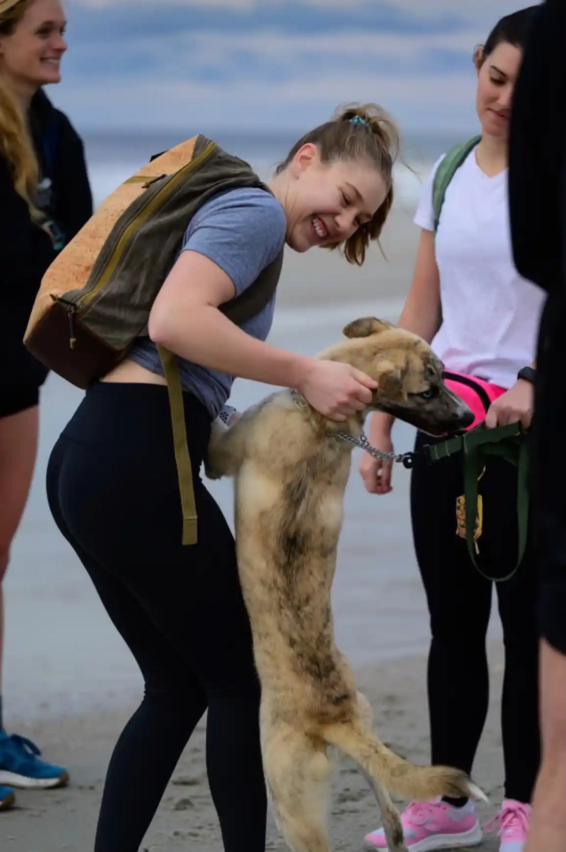 Woman with GORUCK backpack smiling and playing with a dog on a beach, group rucking event