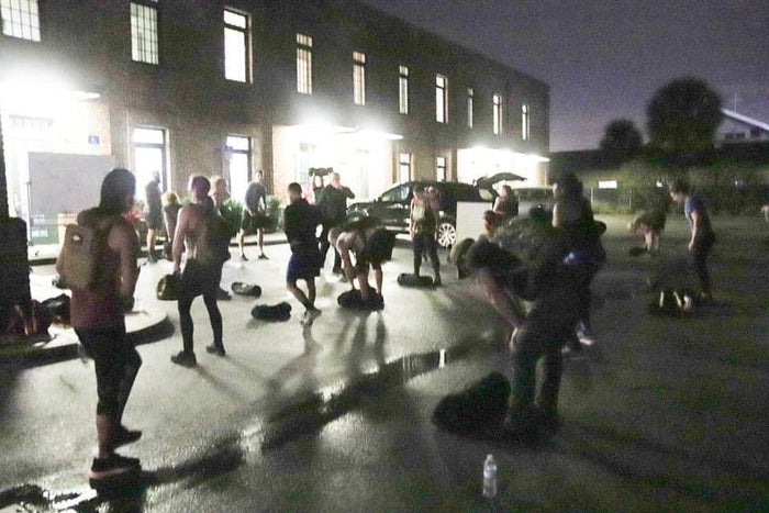 Group of people training outdoors at night doing rucking exercises with backpacks near a building