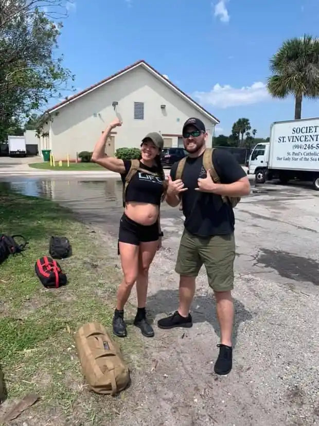 fit man and woman in casual athletic wear and backpacks posing outdoors near a building on a sunny day