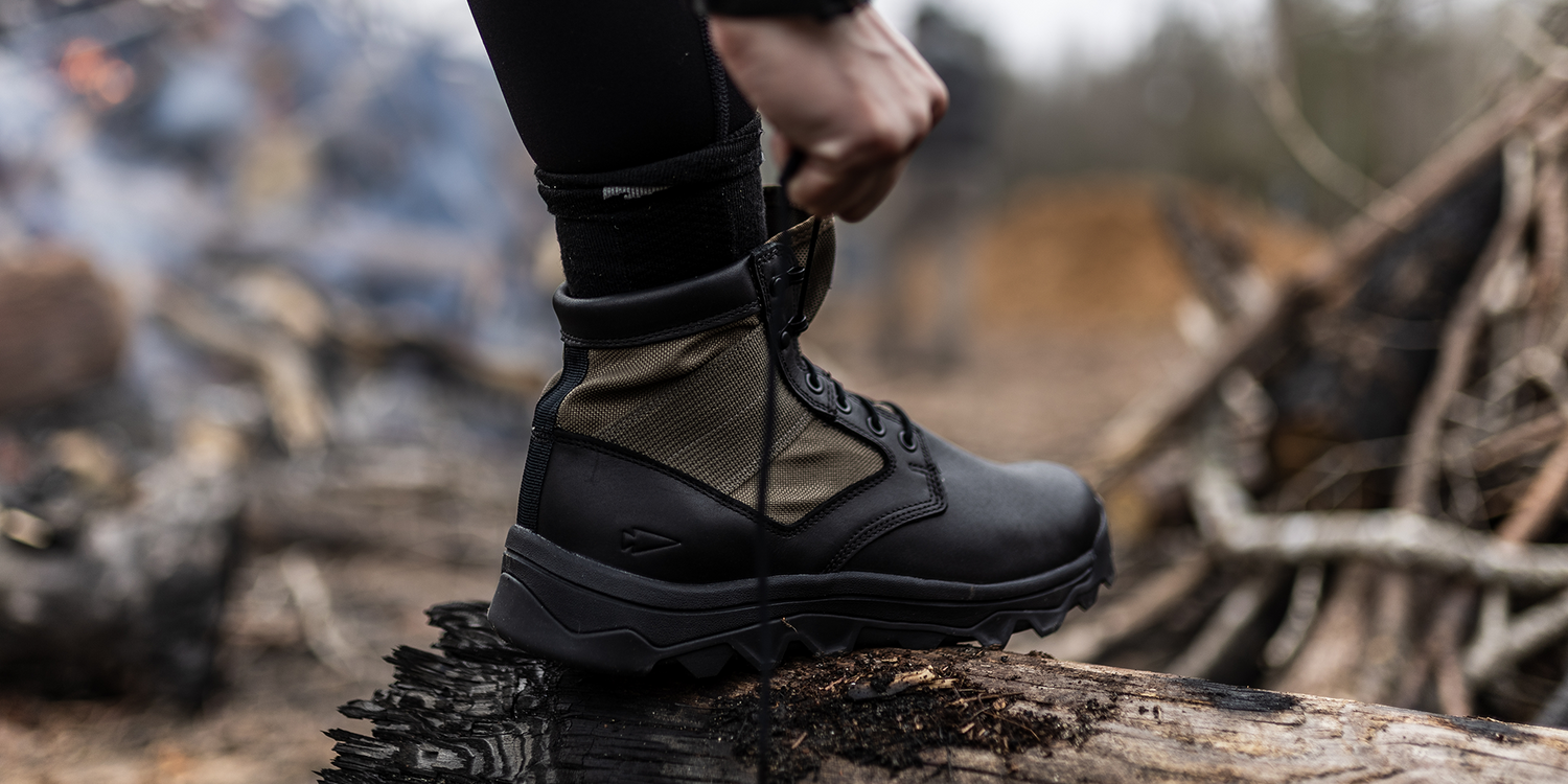 GORUCK rucking boot on a log outdoors, hand tying laces, rugged trail background