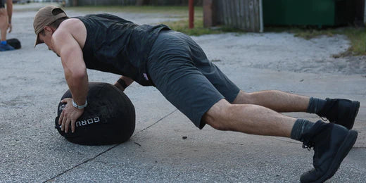 Man in black athletic wear doing push-up exercise on a heavy medicine ball outdoors on concrete