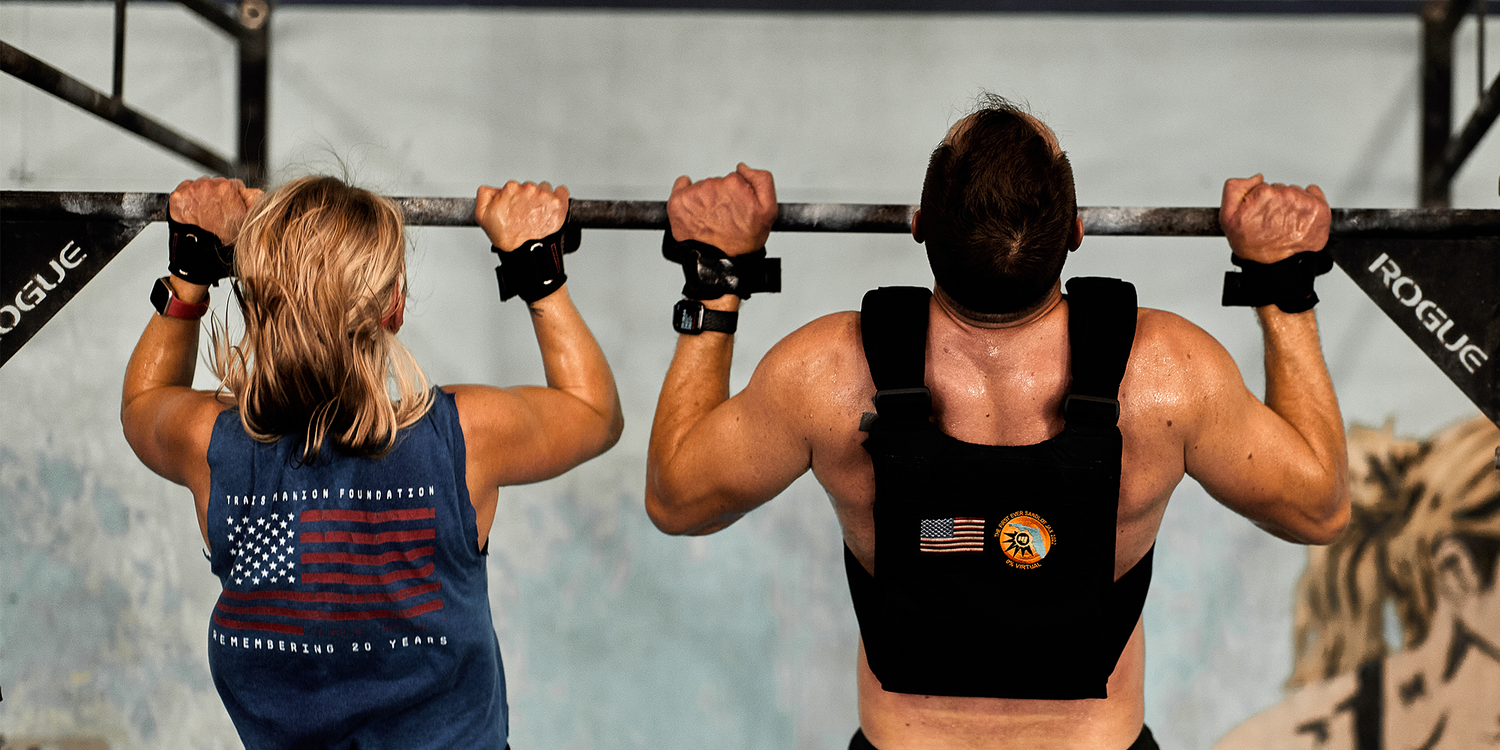 Two athletes doing pull-ups on Rogue bar, wearing GORUCK gear, in gym setting