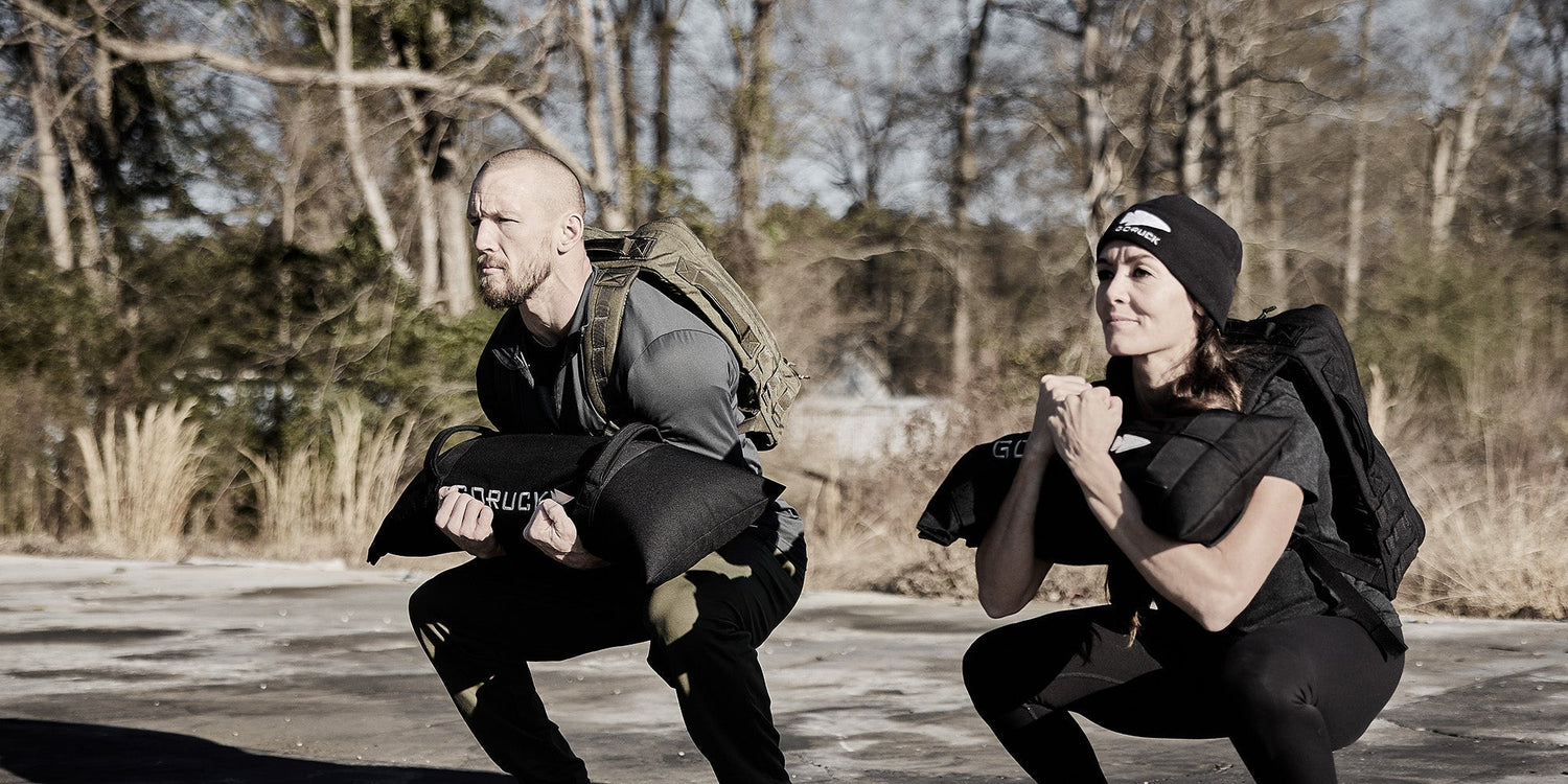 Two people outdoor ruck training with GORUCK gear, backpacks, and weighted bags