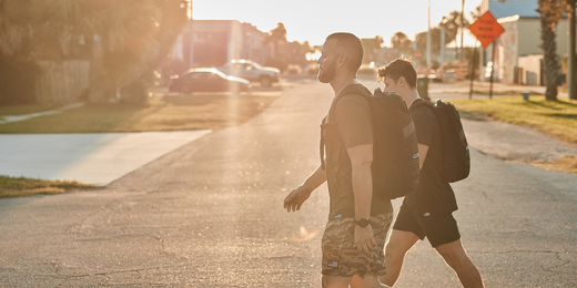Two men walking outdoors wearing GORUCK backpacks in urban setting during sunset for rucking workout