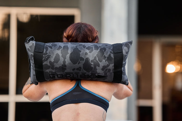 Person lifting a camo GORUCK sandbag for rucking workout outdoors