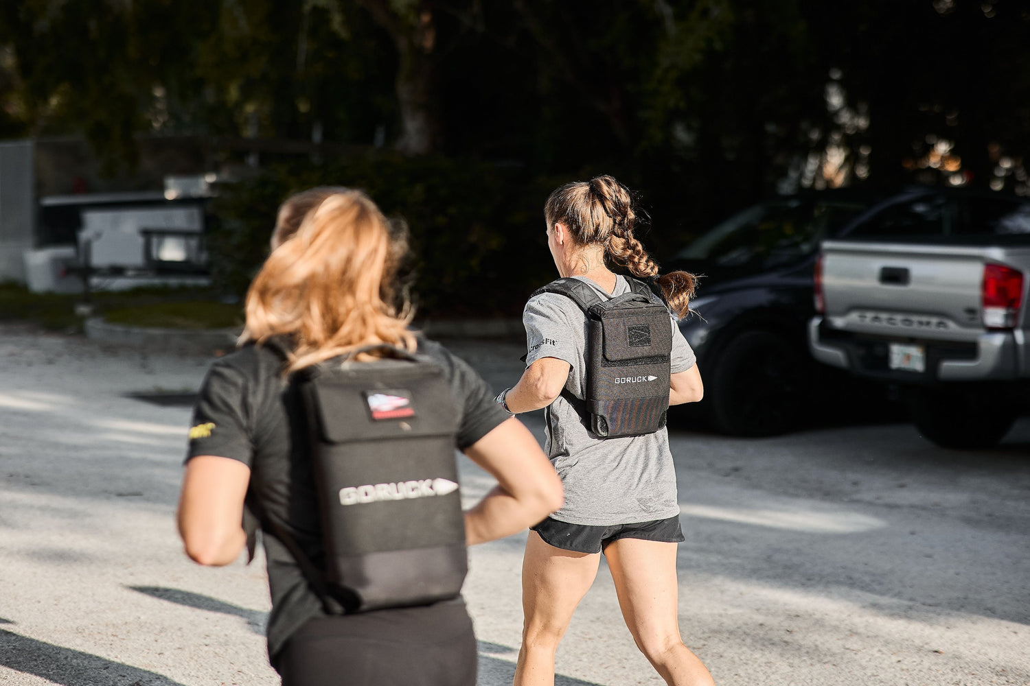 Two women rucking outdoors wearing GORUCK weighted backpacks in a sunny urban setting