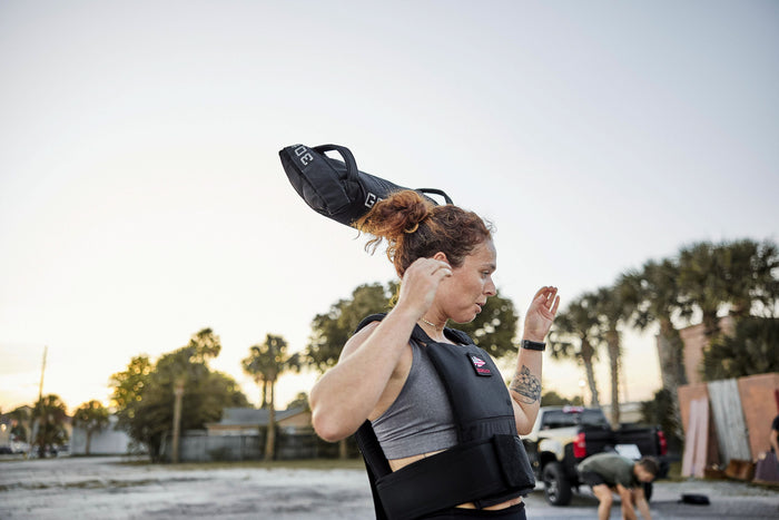 Woman wearing weighted vest lifts GORUCK sandbag outdoors during rucking workout