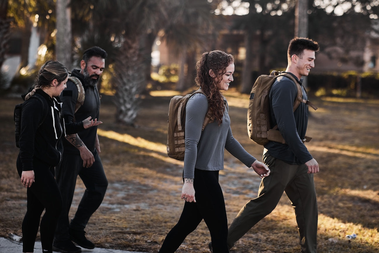 Group rucking outdoors with GORUCK backpacks, smiling and walking through park setting