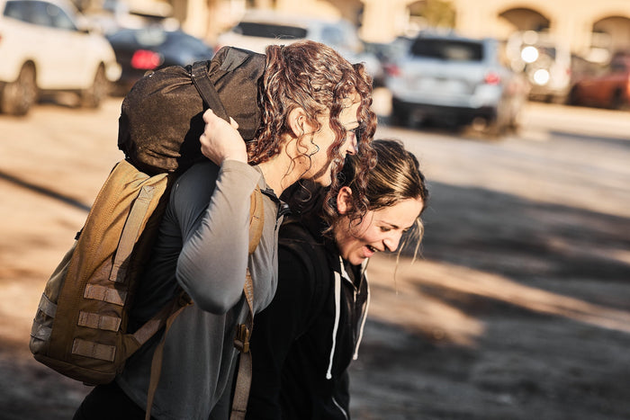 Two women rucking outdoors with GORUCK gear, smiling and carrying backpacks in sunlight