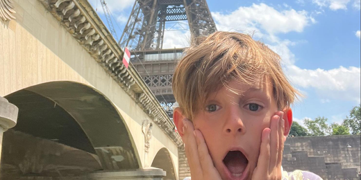 Surprised child with hands on cheeks near Eiffel Tower and Paris bridge on sunny day